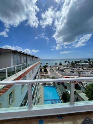 A hotel with a pool, a view of the ocean, and a parking area with cars. - Modern 2BR Penthouse with Jacuzzi & City View (Santo Domingo)