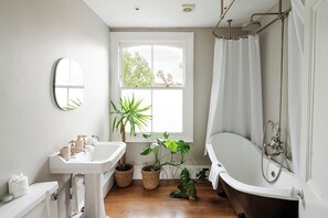 A bathroom with a white sink, a bathtub, a shower, and a window with plants. - Chic Four-Bedroom Townhouse in cool Notting Hill (Greater London)