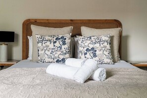 A neatly made bed with floral-patterned pillows, a rolled white towel, and a bedside lamp on a nightstand. - Chic Four-Bedroom Townhouse in cool Notting Hill (Greater London)