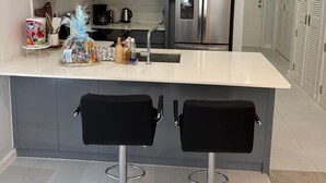 A modern kitchen with a central island, stainless steel appliances, and black bar stools. - Cozy G&C Luxe (Mandeville)