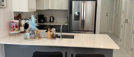 A modern kitchen with a central island, stainless steel appliances, and black bar stools.
