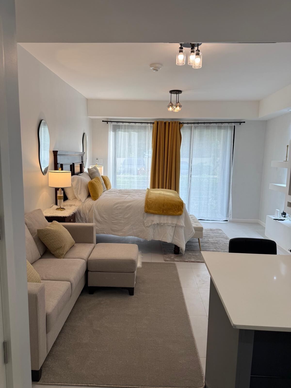 A modern hotel room with a bed, a sofa, a desk, and a large window with curtains.