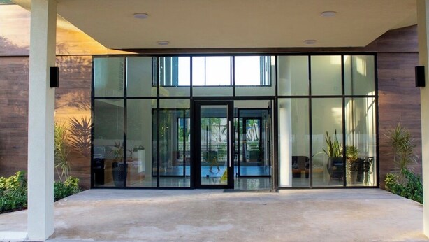 A modern building entrance with glass doors, a concrete walkway, and potted plants. - Cozy G&C Luxe (Mandeville)