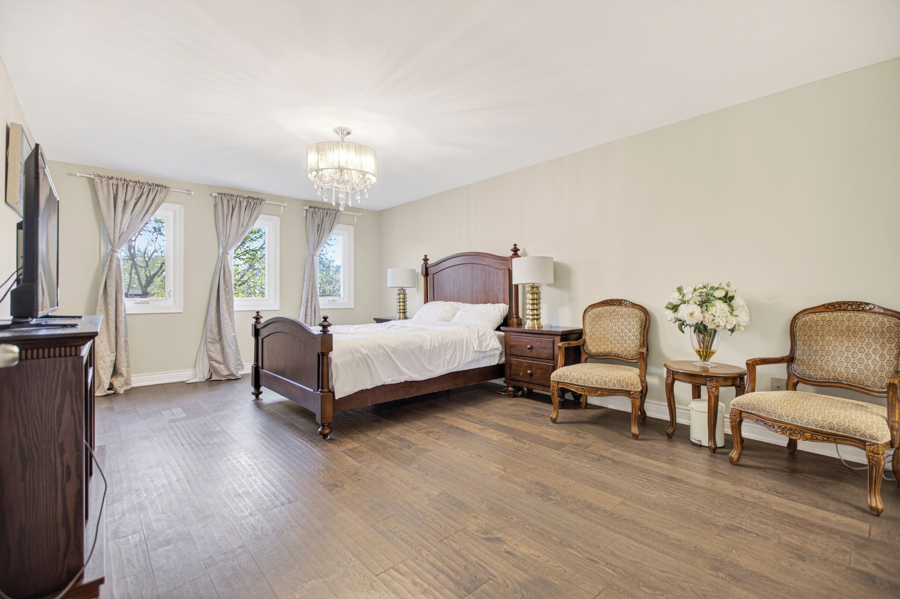 A bedroom with a wooden bed, two chairs, a nightstand, a dresser, and a chandelier.