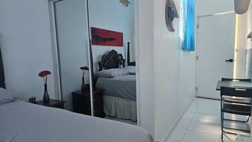 Une chambre à coucher avec un lit, une table de chevet ornée d’un vase, un miroir, une porte donnant sur une autre pièce et une œuvre d’art accrochée au mur.