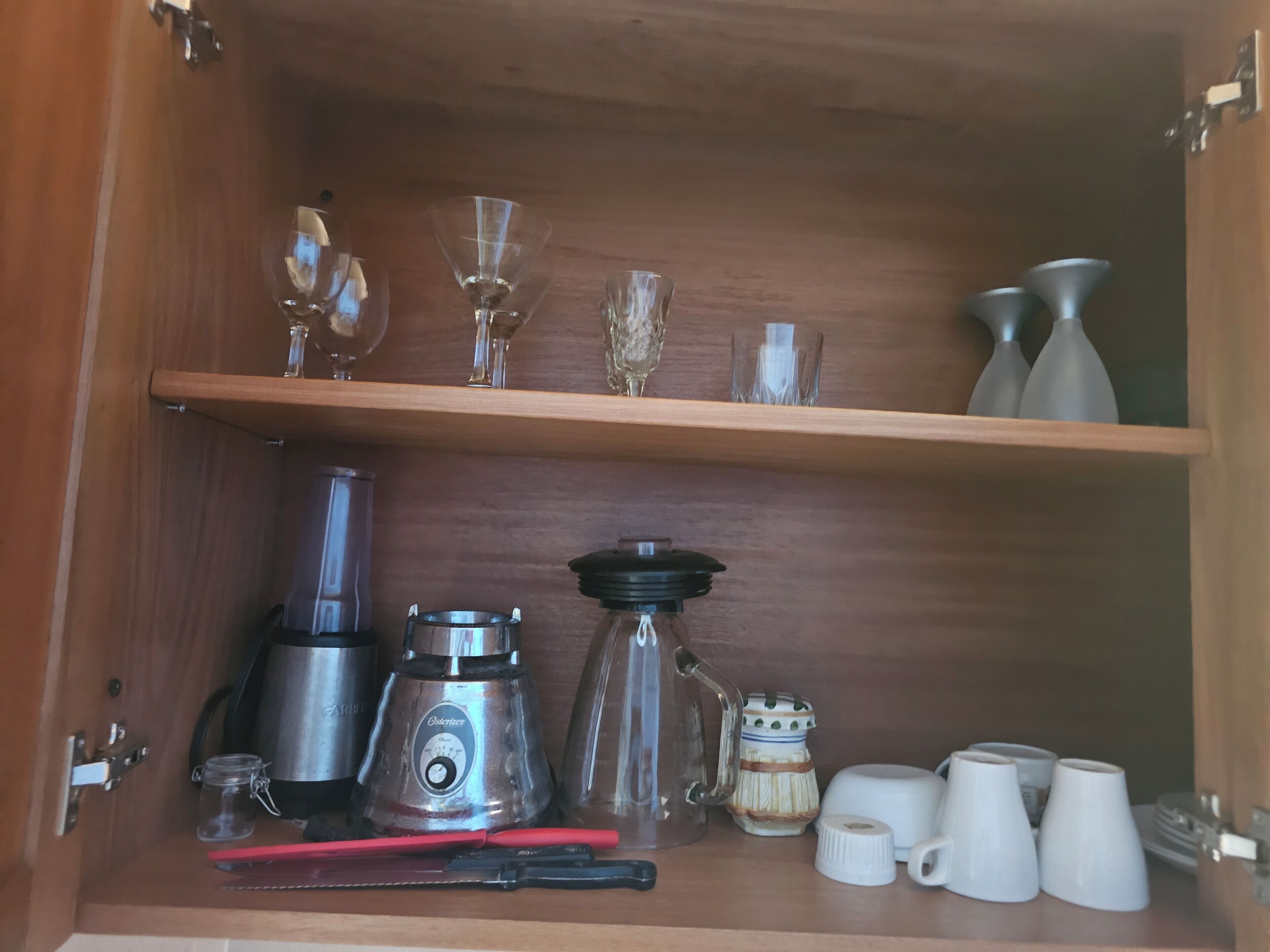 A wooden cabinet with shelves holding various glassware, a coffee maker, and kitchen utensils.