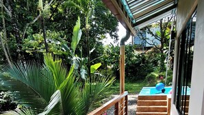 Una terraza de madera con barandilla metálica, una piscina pequeña y abundante follaje.