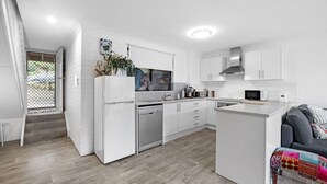 A modern kitchen with white cabinetry, a built-in dishwasher, and a microwave. - The Nook in Mollymook - Walk to the beach! (Mollymook Beach)