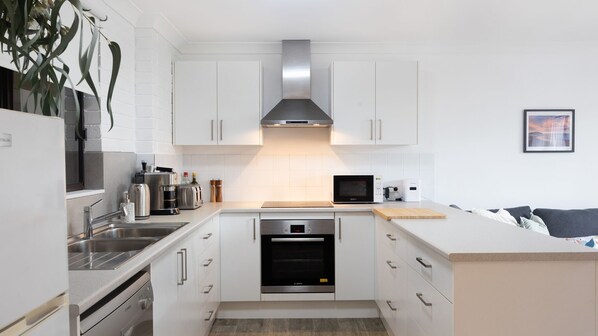 A modern kitchen with white cabinets, stainless steel appliances, and a built-in oven. - The Nook in Mollymook Beach (Mollymook Beach)