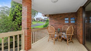 A covered outdoor area with a brick wall, a wooden deck, and wicker chairs. - The Nook in Mollymook Beach (Mollymook Beach)