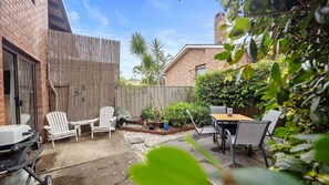 A backyard with a barbecue grill, patio furniture, and a wooden fence. - The Nook in Mollymook Beach (Mollymook Beach)
