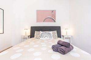 Un lit bien fait, recouvert d’une couvre-lit à pois, avec deux lampes de chevet et un tableau encadré au-dessus du lit.