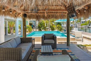 A poolside area with a thatched roof, wicker furniture, and a view of a swimming pool. - Waterfront Pool Home w/ 100' Dock, Tiki Hut & Boating Access Near Key West (Sugarloaf Key)