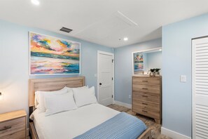A bedroom with a bed, a dresser, a door, and a painting on the wall. - Waterfront Pool Home w/ 100' Dock, Tiki Hut & Boating Access Near Key West (Sugarloaf Key)