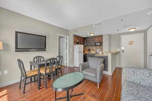 A compact living space with a dining area, a seating area, a kitchenette, and a television mounted on the wall. - Scenic Lakeview Condo w Balcony and Resort Pools (Orlando)