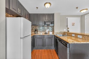 A modern kitchen with dark cabinets, a white refrigerator, a microwave, and a granite countertop. - Scenic Lakeview Condo w Balcony and Resort Pools (Orlando)