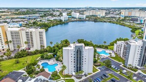A high-rise hotel with a central courtyard pool, surrounded by greenery and other buildings. - Scenic Lakeview Condo w Balcony and Resort Pools (Orlando)