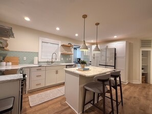 A modern kitchen with a central island, pendant lighting, and a view into the adjacent dining area. - Spacious Raleigh Retreat - 3 BR + Bonus Space - Large Fenced Yard (Raleigh)