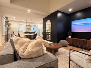 A modern living room with a sofa, coffee table, and a TV displaying a scenic view. - Spacious Raleigh Retreat - 3 BR + Bonus Space - Large Fenced Yard (Raleigh)