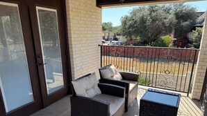 A covered patio area with wicker furniture, a glass door, and a view of a parking lot and trees. - Charming apartment in awesome Mission with cool AC breeze (Mission)