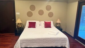 A neatly made bed with white and red bedding, two bedside lamps, a wall with circular decorations, and a wooden floor. - Charming apartment in awesome Mission with cool AC breeze (Mission)