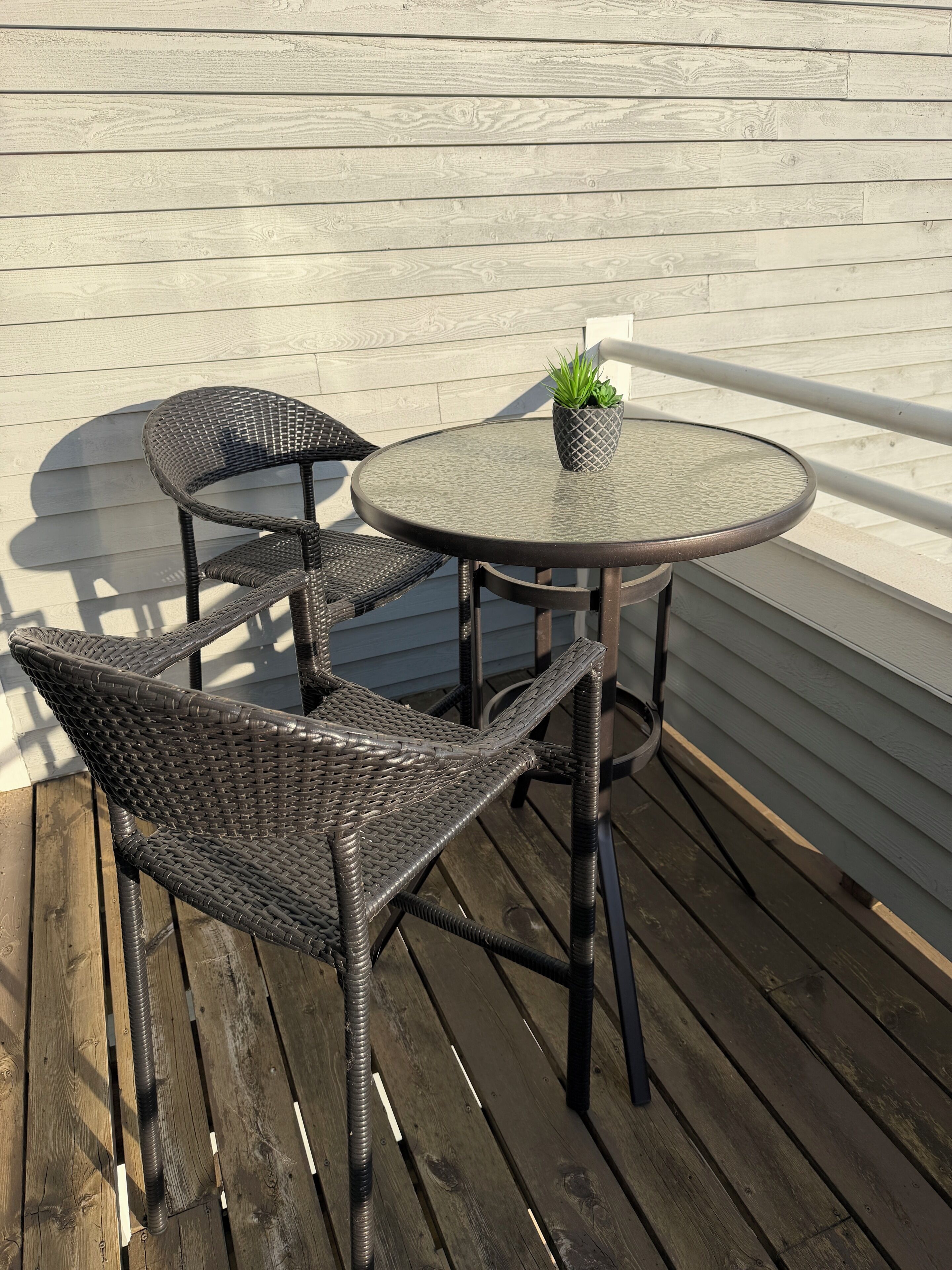 Une table et des chaises en osier sur une terrasse en bois, avec un mur blanc en arrière-plan.