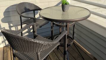 Une table et des chaises en osier sur une terrasse en bois, avec un mur blanc en arrière-plan.