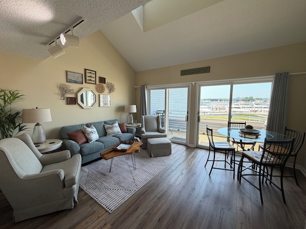 A living room with a sofa, chairs, a coffee table, and a view through a sliding glass door to the outside.