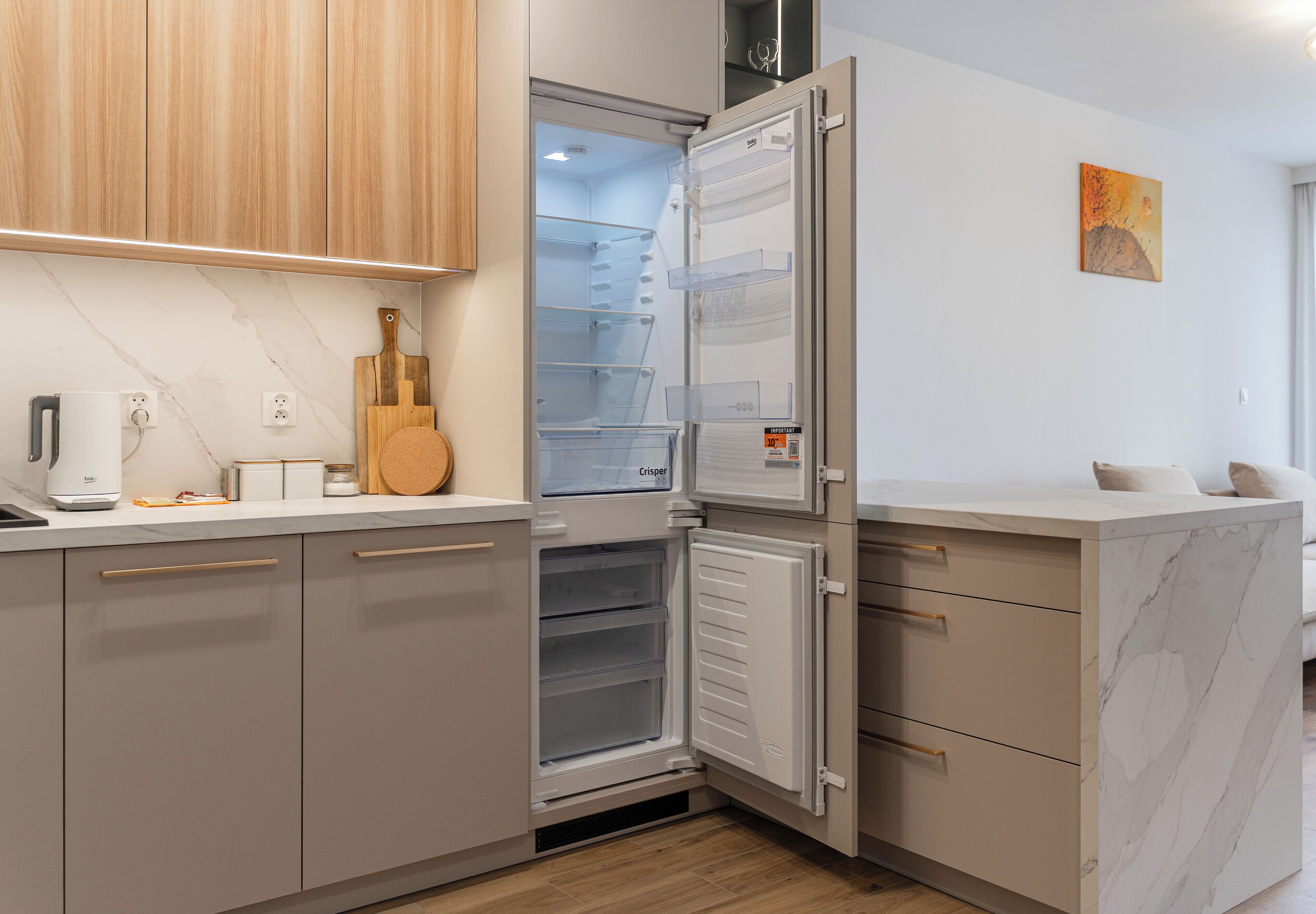 Een moderne keuken met een inbouwkoelkast, houten kastjes en een marmeren aanrecht.
