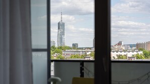 Une pièce avec vue sur un paysage urbain, notamment un immeuble de grande hauteur, visible par une fenêtre.