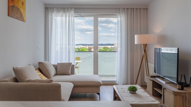 Une chambre d’hôtel moderne, dotée d’un canapé, d’une télévision, d’une lampe et offrant une vue sur la ville grâce à de grandes fenêtres.