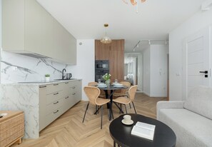 Eine moderne Küche mit Marmorarbeitsplatte, Holzschränken und einem Essbereich mit Korbstühlen und einem schwarzen Tisch.
