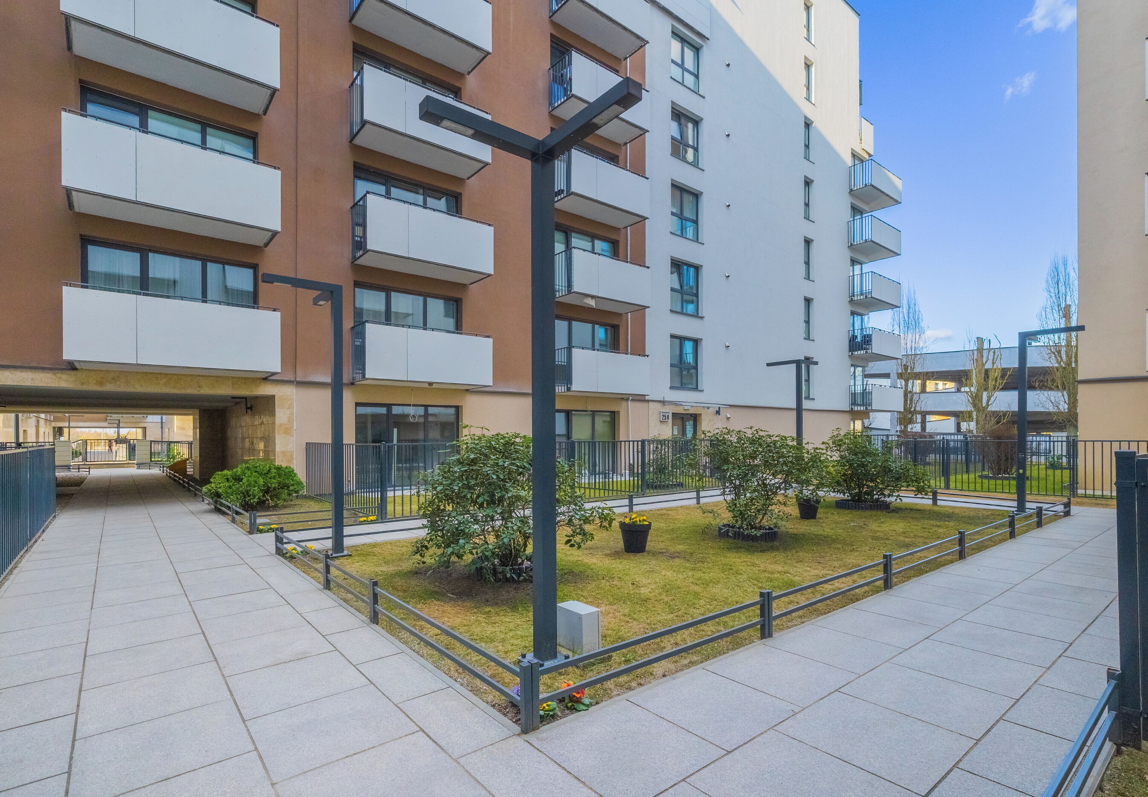 Un edificio residencial de varios pisos con balcones, un patio empedrado y cielo despejado.