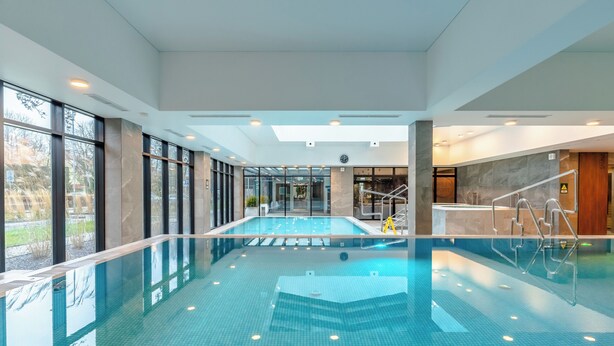 Une piscine intérieure avec des parois en verre transparent, un sol carrelé et un escalier menant à un niveau supérieur.