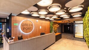 Un comptoir d’accueil avec un panneau circulaire portant l’inscription « GREEN PORT », un mur en bois et un plafond orné de plusieurs luminaires circulaires.
