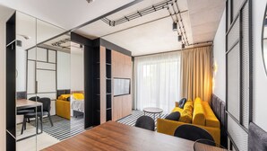 Une chambre d’hôtel moderne avec une table à manger en bois, un canapé, une télévision et une grande fenêtre avec des rideaux.