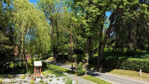 Un sentier dallé, bordé d’une petite construction, le tout entouré d’une végétation luxuriante et d’arbres.