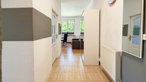 Un couloir avec une porte, un radiateur et une horloge au mur.