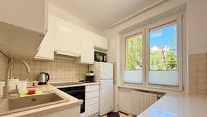 Une cuisine avec un carrelage à motifs, des placards blancs, un évier, une cuisinière et une fenêtre avec des stores.