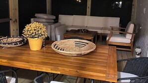 Een terras met een houten tafel, rieten stoelen, een comfortabele bank en een plant in een pot.