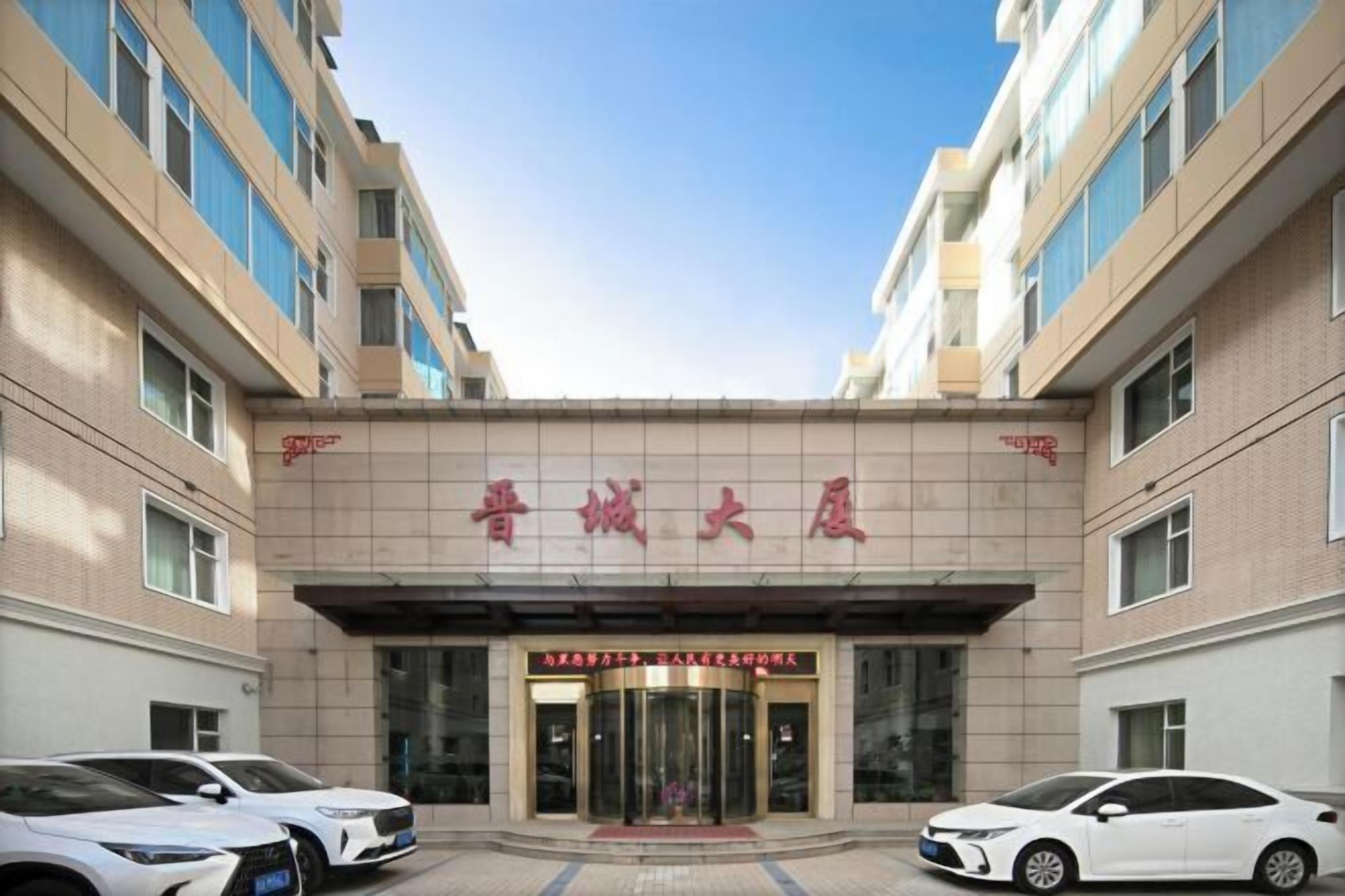A hotel entrance with a sign in a foreign language, a revolving door, and parked cars.