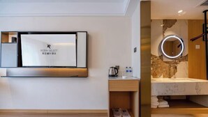 Una habitación de hotel moderna con un televisor de pantalla plana, una tocador de madera con encimera de mármol y un espejo circular.
