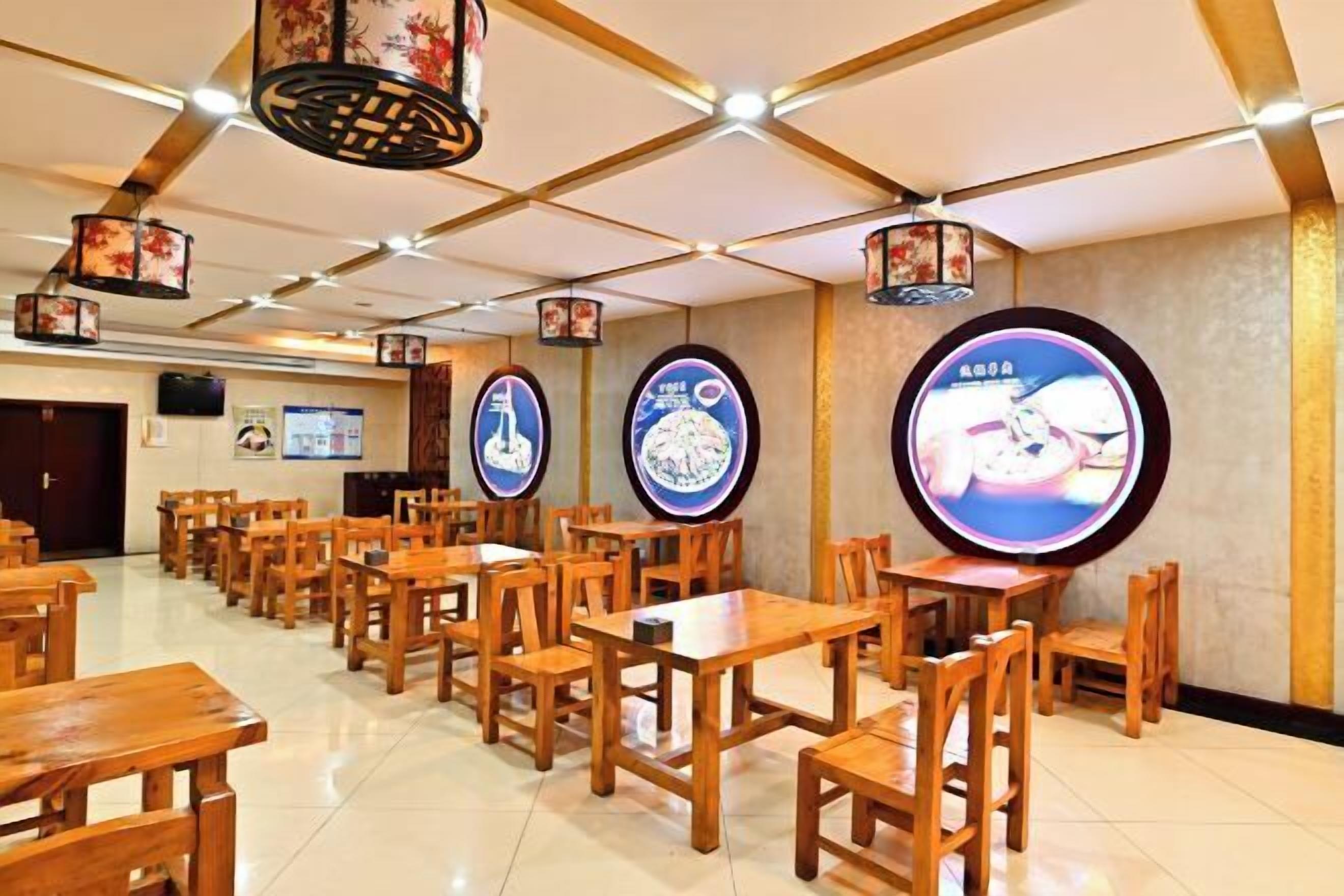A restaurant with wooden tables and chairs, hanging lanterns, and wall-mounted screens displaying images.