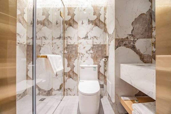 A bathroom with a marble wall, a toilet, a glass shower enclosure, and a marble sink.