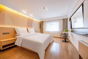 A modern hotel room with a large bed, bedside table, and a small table with a plant.