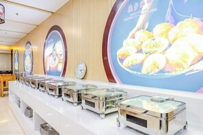 A buffet area with multiple glass display cases containing food, a wall with clocks, and a large poster of food items.