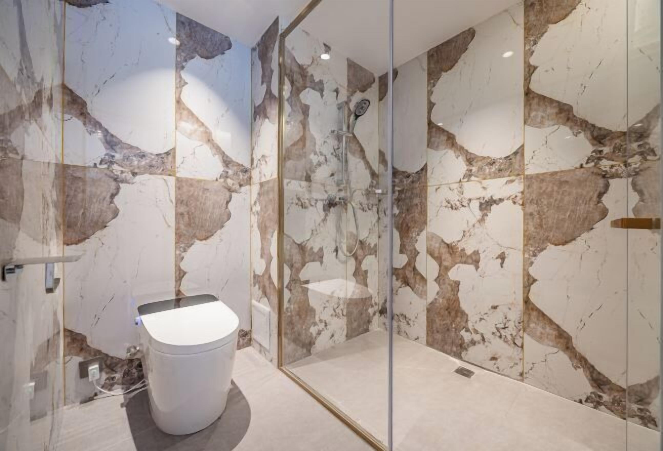 Een badkamer met een glazen douchecabine, toilet en marmeren wanden.