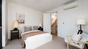 Ein Schlafzimmer mit Bett, Nachttischen, einem Sessel, einer Treppe und einer Klimaanlage.