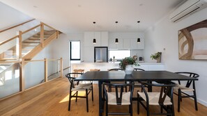 Eine moderne Küche mit weißen Schränken, ein Essbereich mit schwarzem Tisch und Stühlen sowie eine Holztreppe.