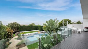 A rooftop pool area with a glass balustrade, a small slide, and a seating area with a table and chairs.